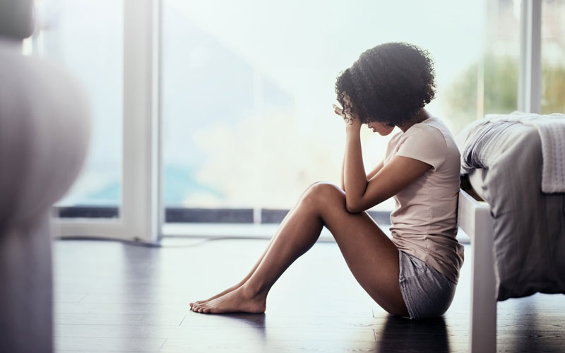 woman sitting at the edge of her bed seemingly upset