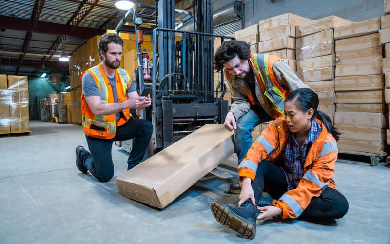 woman holding her ankle in pain by a forklift