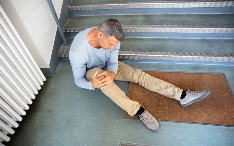 man holding his knee in pain at the bottom of stairs