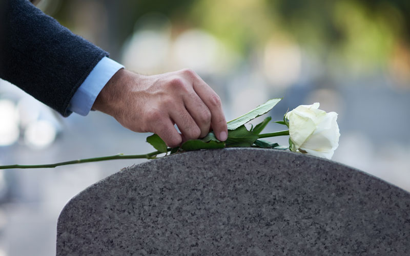 man placing a flower on a grave